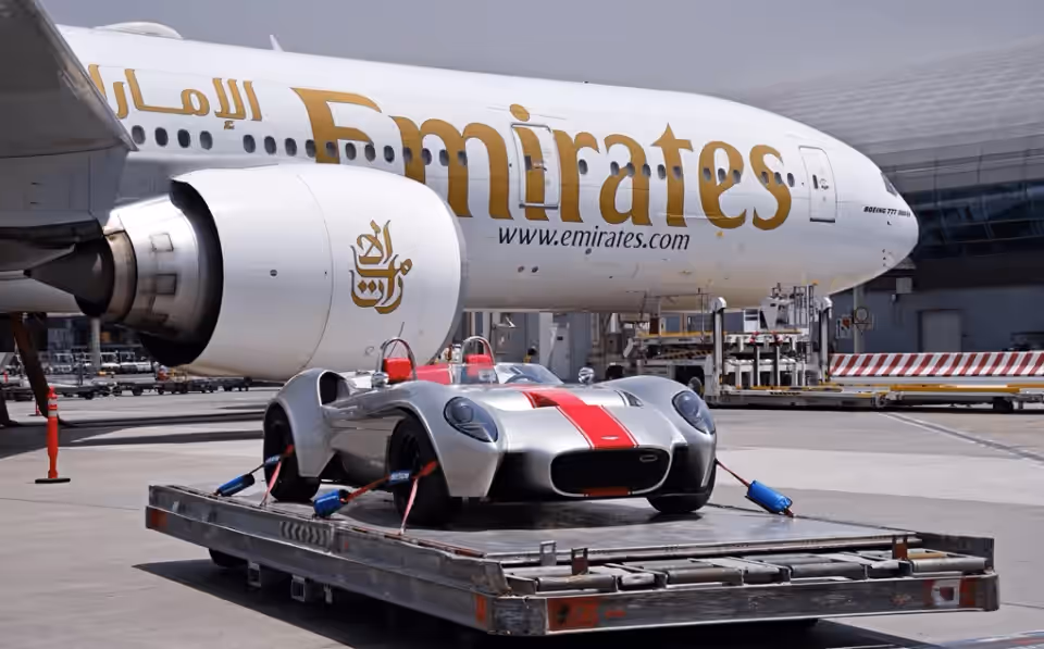 Race car on an air cargo pallet beside an Emirates freighter