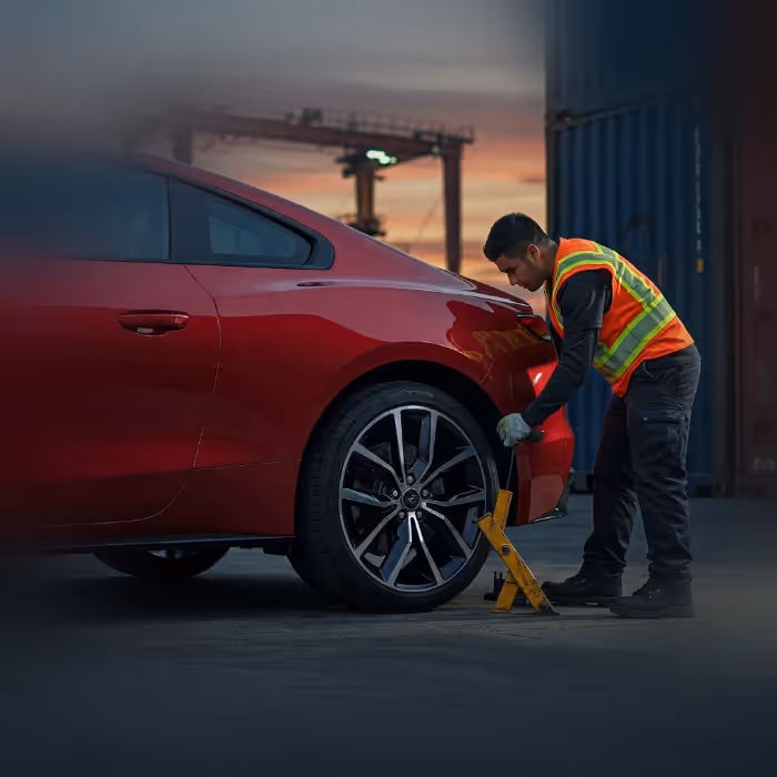 Worker securing the wheel of a red car before shipping